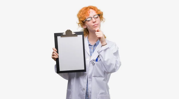 Jeune Rousse Médecin Femme Tenant Presse Papiers Visage Sérieux Penser — Photo