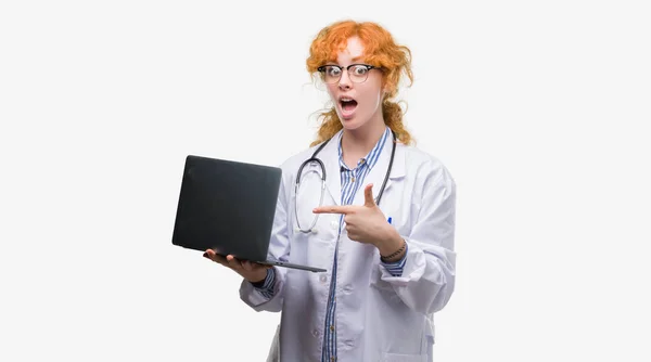 Młoda Ruda Kobieta Lekarz Trzymając Komputer Laptop Bardzo Szczęśliwy Wskazując — Zdjęcie stockowe
