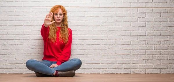 レンガ壁を停止歌う手のひらに座っている赤毛の若い女性 顔に否定的な深刻なジェスチャーで警告式 — ストック写真
