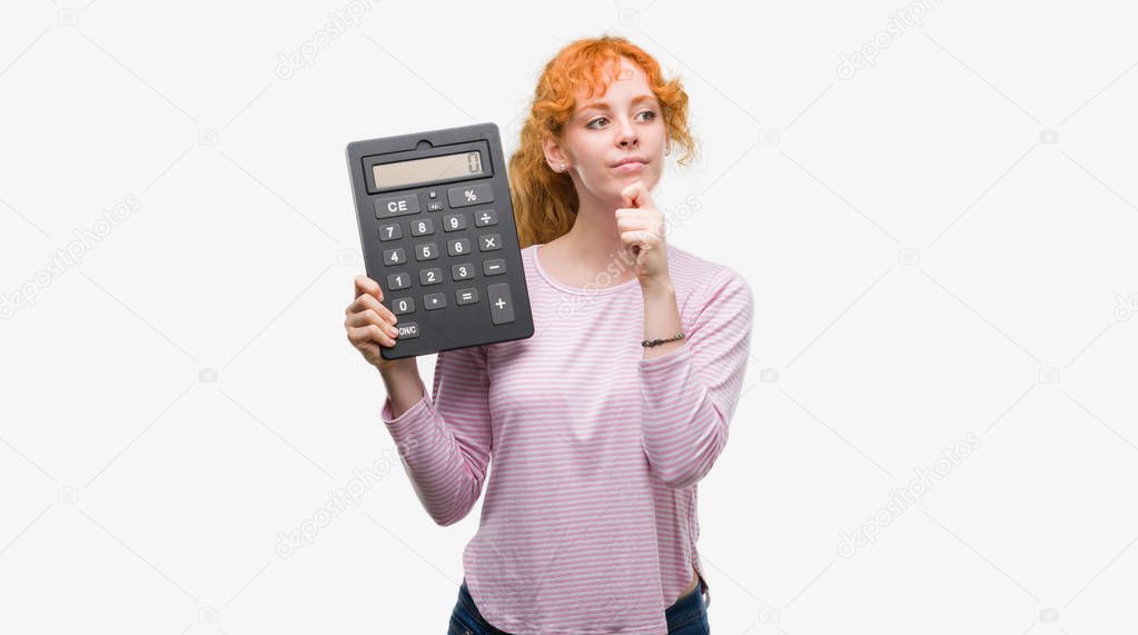 Young redhead woman holding big calculator serious face thinking about question, very confused idea
