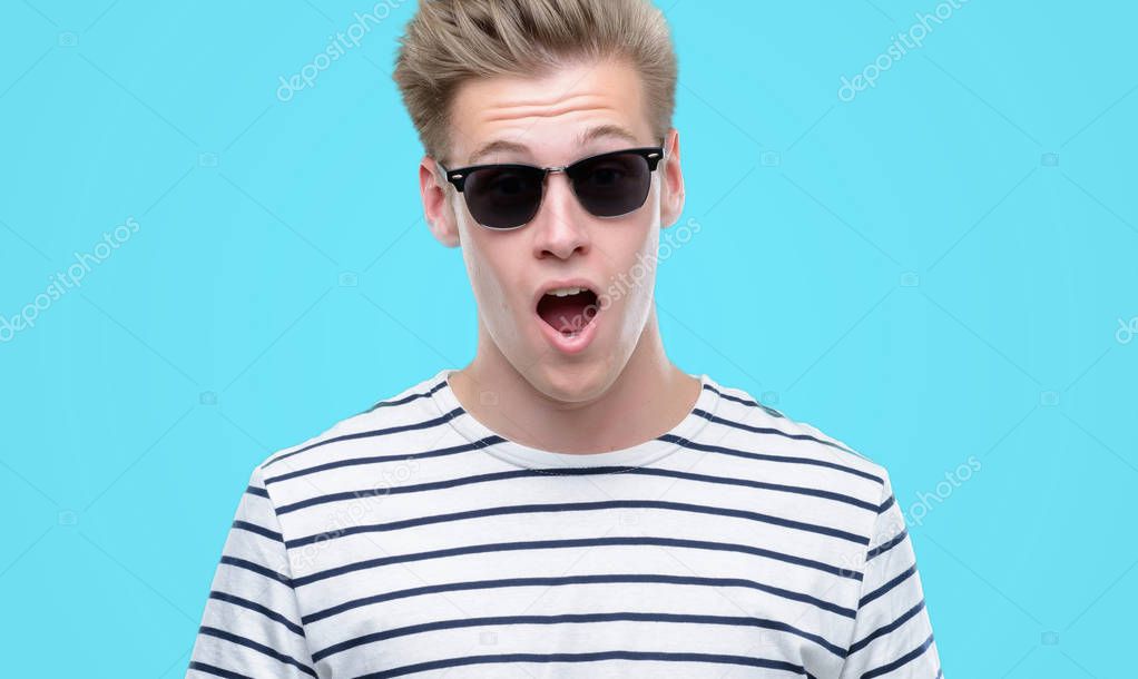 Young handsome blond man wearing sunglasess scared in shock with a surprise face, afraid and excited with fear expression