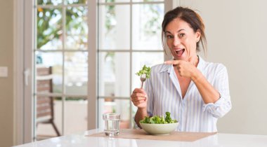 Orta yaşlı kadın evde çok mutlu el ve parmak ile işaret bir kase taze salata yemek