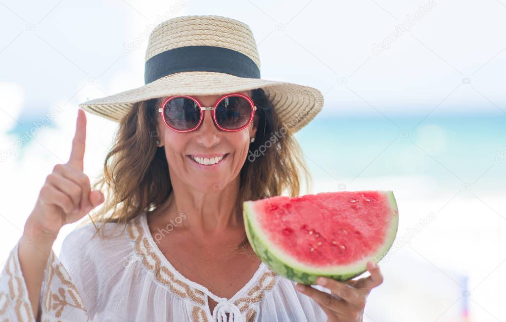 Middle age brunette woman by the sea eating watermelon surprised with an idea or question pointing finger with happy face, number one
