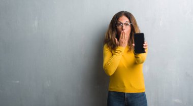 Orta yaş İspanyol kadın smarphone ekran kapağı ağız el ile şok utançla hata, korku, ifade için gösterilen sessizlik içinde gizli kavramı korkuttu