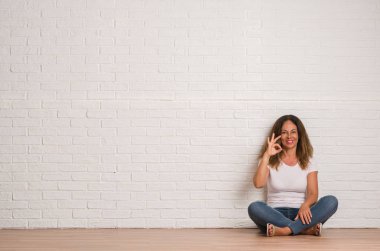 Orta yaş İspanyol kadın parmakları, mükemmel sembolü olan ok işareti yapıyor beyaz tuğla duvarın üzerinden