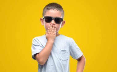 Koyu saçlı küçük çocuk giyen güneş gözlüğü el hata, korku, sessizlik içinde gizli kavramı korkmuş ifade için utanç ile şok ile ağız kapak