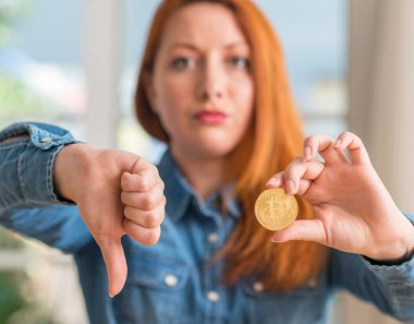 Kızgın yüz, eksi işareti aşağı antipati başparmak ile gösterilen, ret kavramı ile Bitcoin cryptocurrency evde tutan Kızıl saçlı kadın