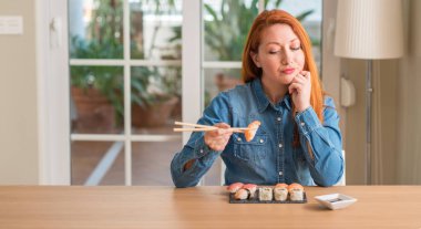 Yemek çubukları ciddi bir yüz düşünme hakkında soru, çok karışık bir fikir kullanarak suşi yemek Kızıl saçlı kadın