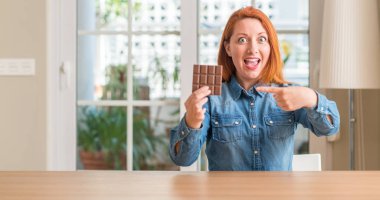 Ev çok mutlu el ve parmak ile işaret çikolata bar tutan Kızıl saçlı kadın