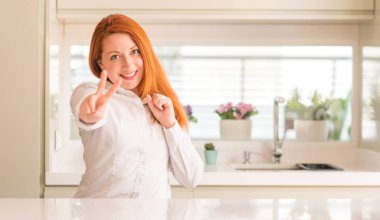 Zafer işareti yapıyor parmak gösterilen kamera seyir gülümseyen mutfak Kızıl saçlı kadın. İki numaralı.