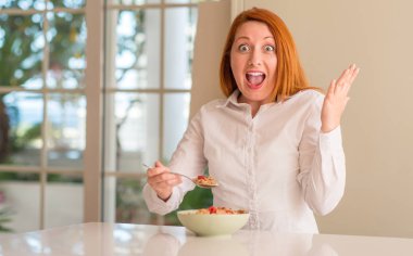 Ahududu evde çok mutlu ve heyecanlı, kocaman bir gülümseme ile çığlık zaferini kutluyor kazanan ifade ile tahıl yemek ve ellerini kaldırdı Kızıl saçlı kadın