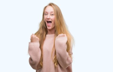 Kutlayan pembe kazak giymiş sarışın genç kadın şaşırttı ve başarı için kaldırdı kollarını açarak hayret ve gözleri açık. Kazanan kavramı.