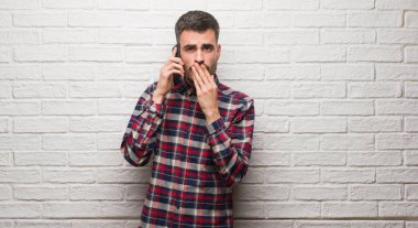 Hata, korku, sessizlik içinde gizli kavramı korkmuş ifade için utanç ile beyaz tuğla duvar kapağı ağız el ile üzerinden telefon ayakta konuşan genç yetişkin adam şok