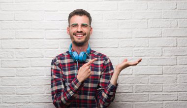 El ve parmak ile işaret çok mutlu kulaklıklar giyen tuğla duvarın üzerinden genç yetişkin adam