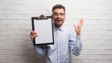 Genç Yetişkin iş adamı ile çığlık zaferini kutluyor Pano çok mutlu ve heyecanlı, kazanan ifade büyük holding tuğla duvarın üzerinden gülümse ve el kaldırdı