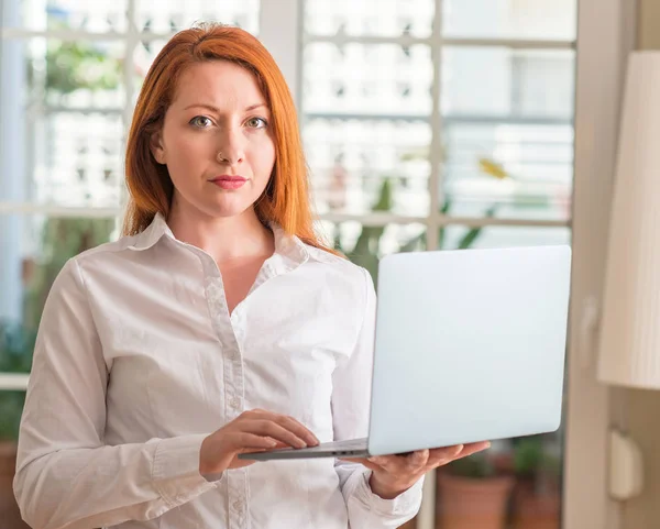 红发女子在家里用电脑膝上型计算机 自信的表情对聪明的面孔认真思考 — 图库照片