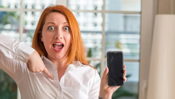 Donna Rossa Utilizzando Smartphone Casa Con Faccia Sorpresa Puntando Dito — Foto Stock