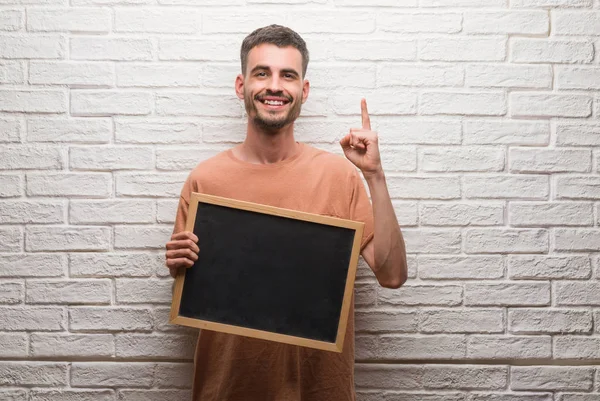 Joven Adulto Sobre Pared Ladrillo Sosteniendo Pizarra Sorprendido Con Una — Foto de Stock