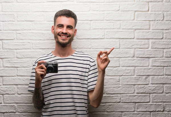 若い男側の手と指で指す非常に幸せの白いレンガの壁にヴィンテージカメラ立ってを保持しています — ストック写真