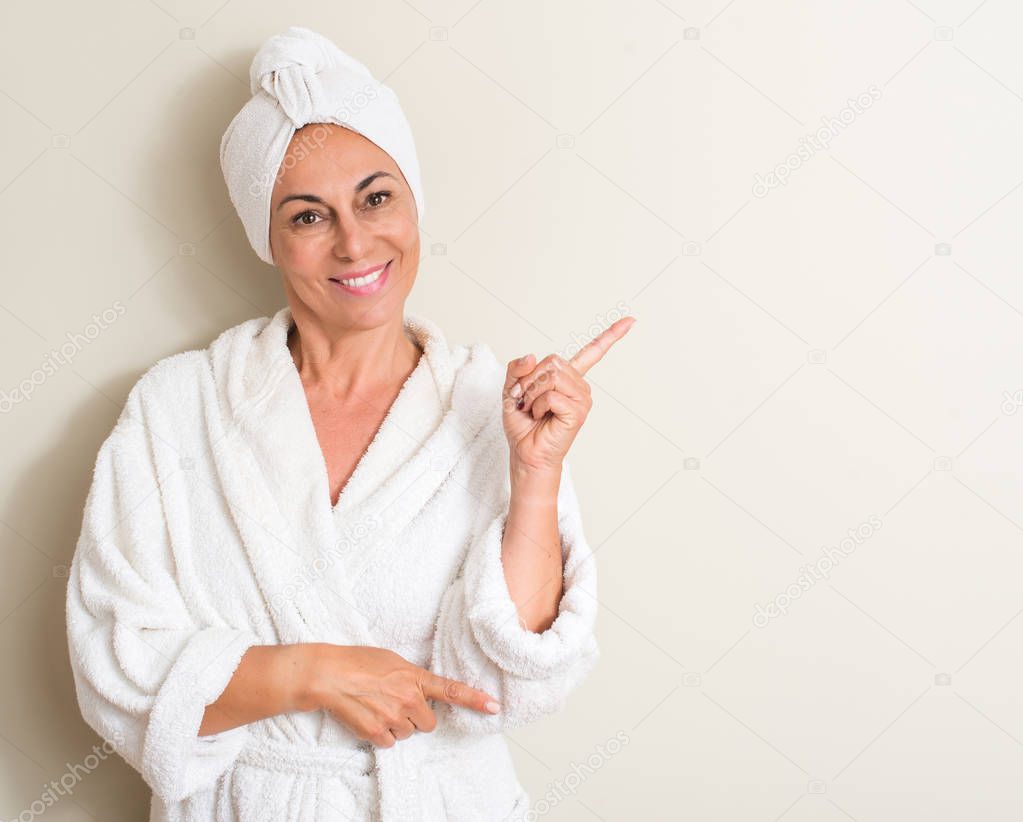 Beautiful middle age woman, wet hair wearing a towel very happy pointing with hand and finger to the side