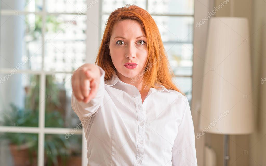 Redhead woman wearing white shirt at home pointing with finger to the camera and to you, hand sign, positive and confident gesture from the front