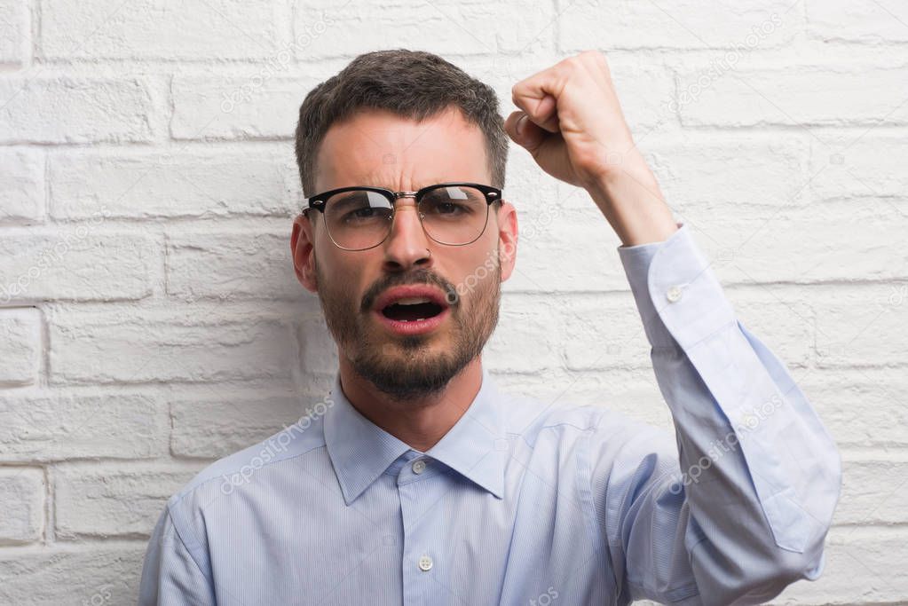 Young adult business man standing over white brick wall annoyed and frustrated shouting with anger, crazy and yelling with raised hand, anger concept