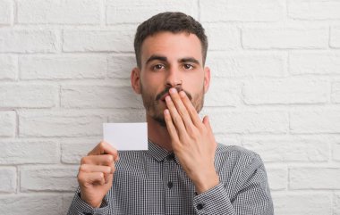 Hata, korku, sessizlik içinde gizli kavramı korkmuş ifade için utanç ile boş kartı kapak ağız eliyle tutarak tuğla duvarın üzerinden genç yetişkin adam şok