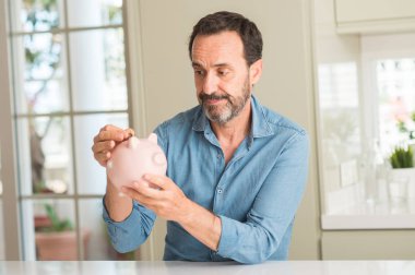 Orta yaş erkek ile acımak yüz düşünme ciddi kendine güvenen bir ifade piggy banka üzerinde tasarruf