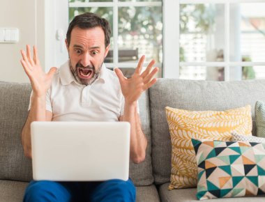 Dizüstü bilgisayar kullanan büyük gülümseme ile çığlık ve ellerini kaldırdı zaferini kutluyor kanepe çok mutlu ve heyecanlı, kazanan ifade orta yaş adam