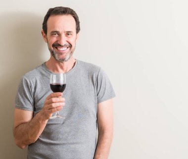 Komuta sizde ayakta ve diş gösterilen kendine güvenen bir gülümsemeyle gülümseyerek mutlu bir yüz ile bir bardak kırmızı şarap içme