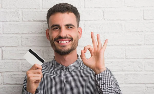 Joven Hombre Adulto Sobre Pared Ladrillo Celebración Tarjeta Crédito Haciendo —  Fotos de Stock