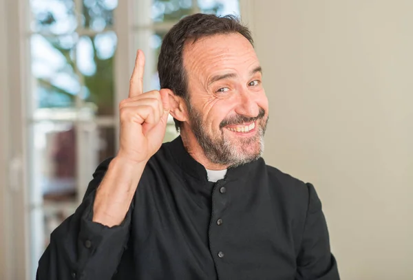 Christian priest man surprised with an idea or question pointing finger with happy face, number one