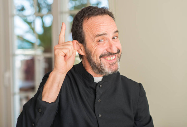 Christian priest man surprised with an idea or question pointing finger with happy face, number one