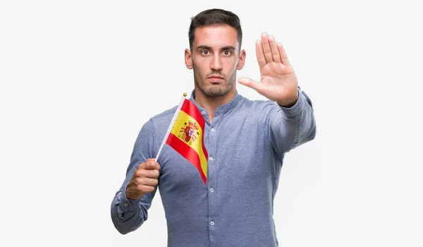 付いているスペインの旗を保持しているハンサムな若い男が防衛ジェスチャー 深刻な自信を持って式に一時停止の標識をやって手を開いてください — ストック写真