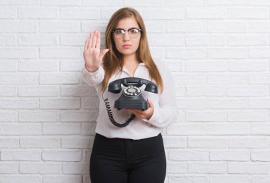 Genç Yetişkin kadın vintage telefonla holding beyaz tuğla duvarın üzerinden açık el dur işareti ile ciddi ve kendine güvenen ifade, savunma hareketi yapıyor