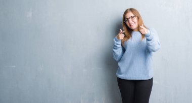 Gri grunge duvar fotoğraf makinesi ile mutlu ve komik yüz için parmakları işaret gözlüklü Genç Yetişkin kadın. İyi enerji ve vibes.