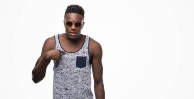 Genç Afro-Amerikan adam kendisi için sürpriz yüz işaret parmağı ile güneş gözlüğü takıyor