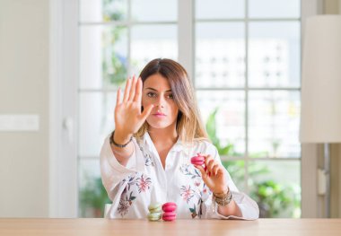 Genç kadın evde açık eliyle dur işareti ile ifade, ciddi ve kendinden emin yapıyor macarons yeme savunma hareketi