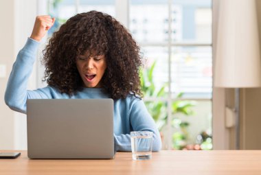 Dizüstü bilgisayar kullanan ev rahatsız ve hayal kırıklığı ile öfke, çılgın ve yükseltilmiş eliyle diye bağıran öfke kavramı bağırarak Afrikalı-Amerikalı kadın