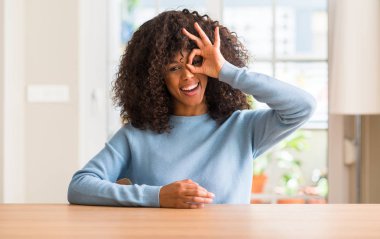 Afrikalı-Amerikalı kadın evde gülümseyen, parmakları ile mutlu yüz üzerinden seyir göz el ile ok jest yapıyor.