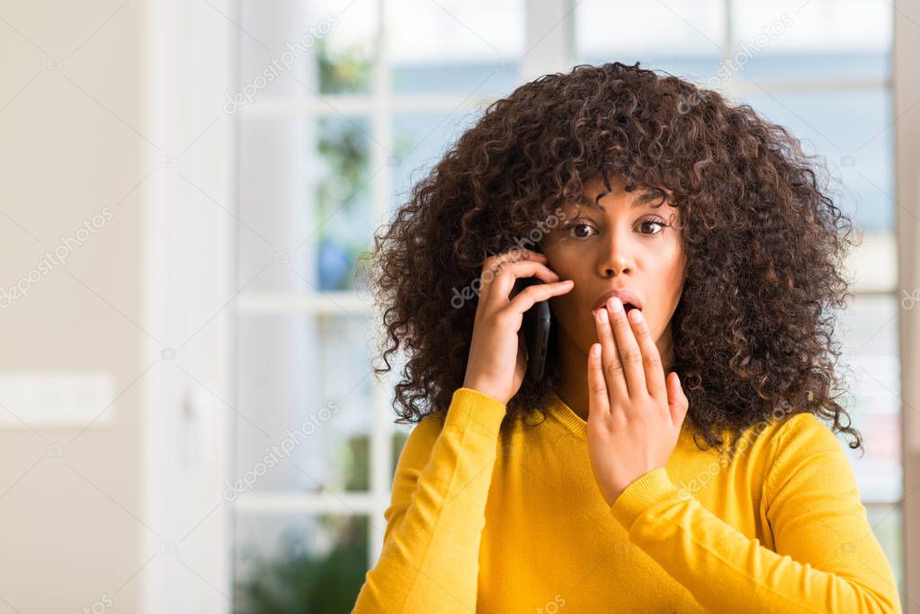 African american woman using smartphone cover mouth with hand shocked with shame for mistake, expression of fear, scared in silence, secret concept