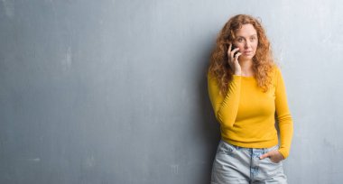 Acımak yüz ciddi düşünüyorum üstünde kendine güvenen bir ifade ile telefonda konuşurken gri grunge duvarın üzerinden genç Kızıl saçlı kadın
