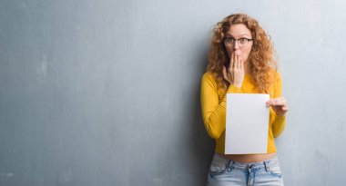 Hata, korku, sessizlik içinde gizli kavramı korkmuş ifade için utanç ile genç Kızıl saçlı kadın boş kağıt sayfası kapak ağız eliyle tutarak gri grunge duvarın üzerinden şok