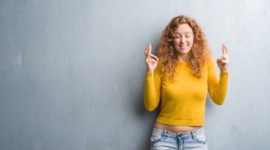 Gri grunge duvar geçiş parmakları umut ve gözleri kapalı ile gülümseyen genç Kızıl saçlı kadın. Şans ve batıl kavramı.