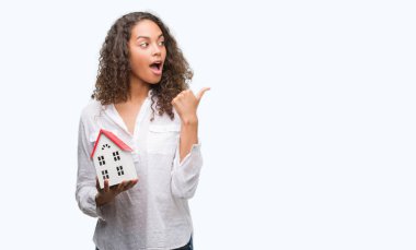 İşaret ve başparmak kadar mutlu yüz gülümseyen tarafı ile gösterilen küçük ev tutan genç İspanyol gerçek durum Aracısı kadın