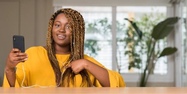 Afrikalı-Amerikalı kadın kendisine sürpriz yüz işaret parmağı ile kulaklıklar ile Smartphone kullanarak