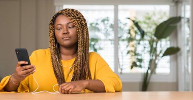 Acımak yüz ciddi düşünüyorum üstünde kendine güvenen bir ifade ile kulaklık ile akıllı telefon kullanan Afrikalı-Amerikalı kadın