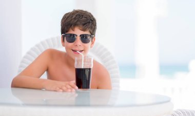Ayakta ve diş gösterilen kendine güvenen bir gülümsemeyle gülümseyerek mutlu bir yüz ile soda içme tatil günlerinde genç çocuk