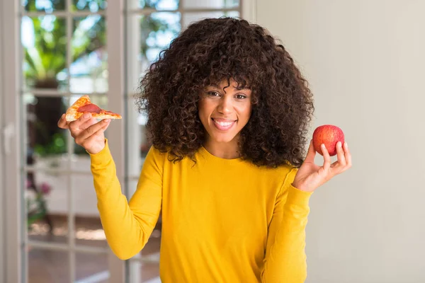 非洲裔美国妇女选择在苹果和比萨饼切片与一个快乐的脸站在微笑着自信的微笑显示牙齿 — 图库照片