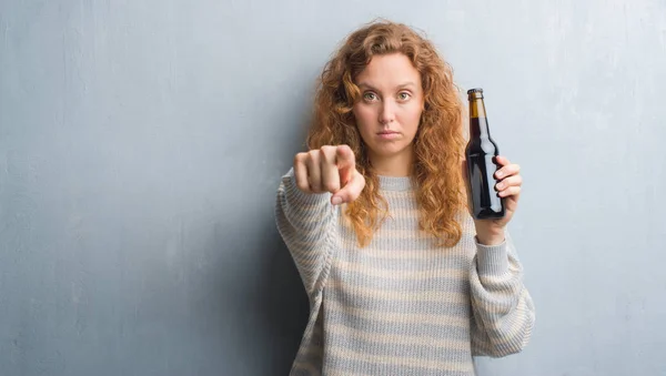 Joven Pelirroja Sobre Pared Grunge Gris Sosteniendo Botella Cerveza Apuntando — Foto de Stock